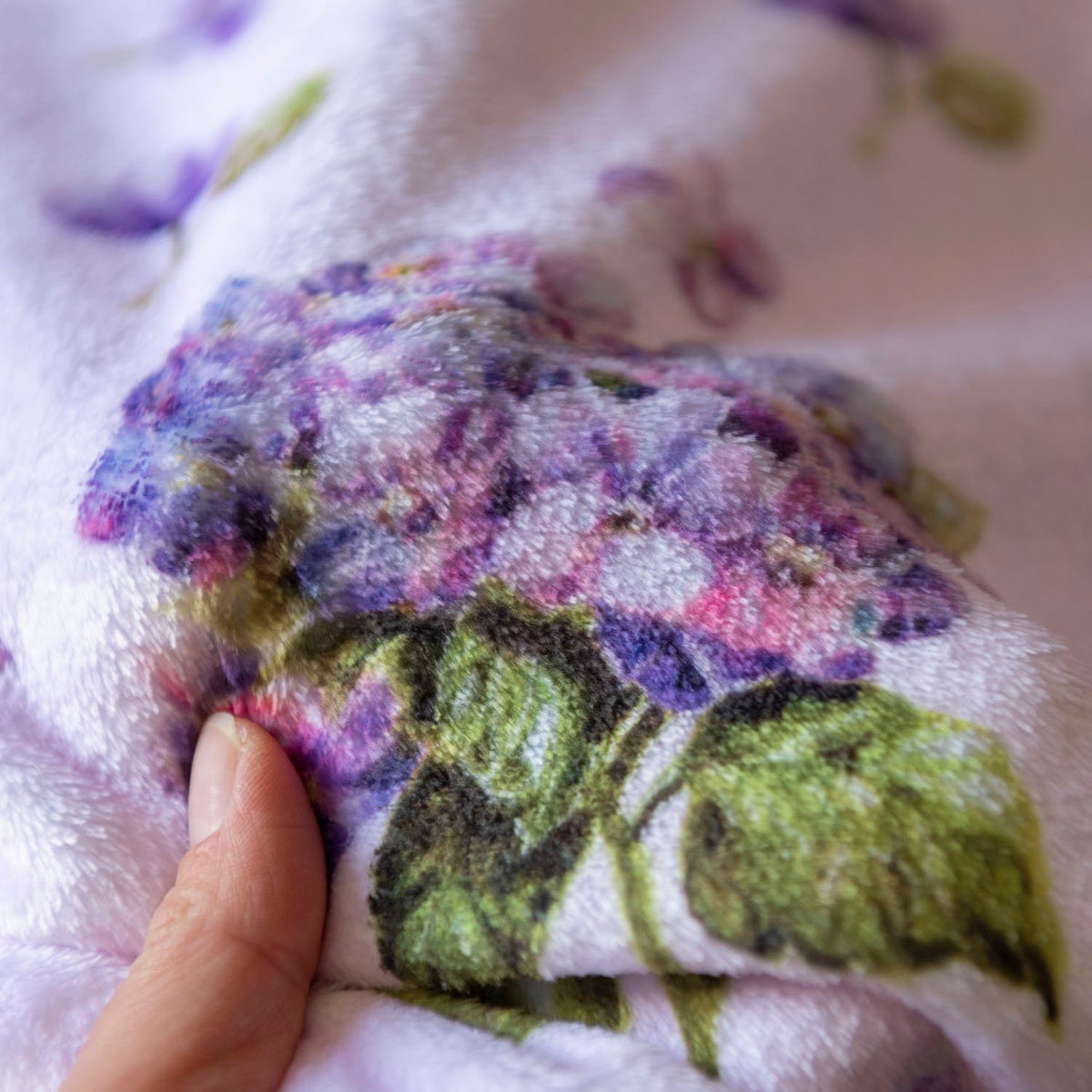 Hand pressing soft hydrangea-print plush fabric to show its fuzzy texture.