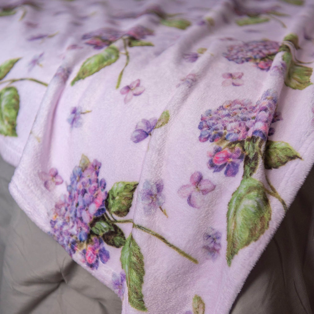 Purple hydrangea plush blanket draped over a grey surface in soft light.