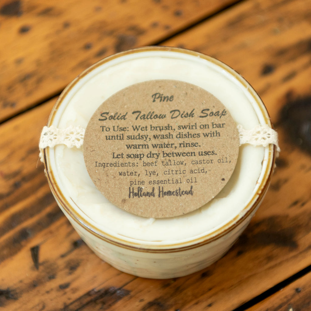 A jar of fine solid beef tallow soap by Holland Homestead, wrapped in white ribbon with a kraft paper label, placed on a rustic wooden surface.